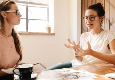 Two young female creative professionals discuss and idea. They are dressed casually and wearing glasses